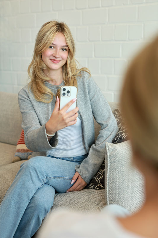Junge Frau sitzt auf dem Sofa und fotografiert mit einem Handy. 